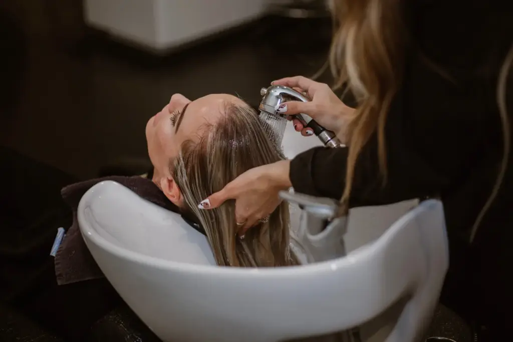 A person is getting their hair washed at a salon basin by another person, showcasing haircare and the salon experience.