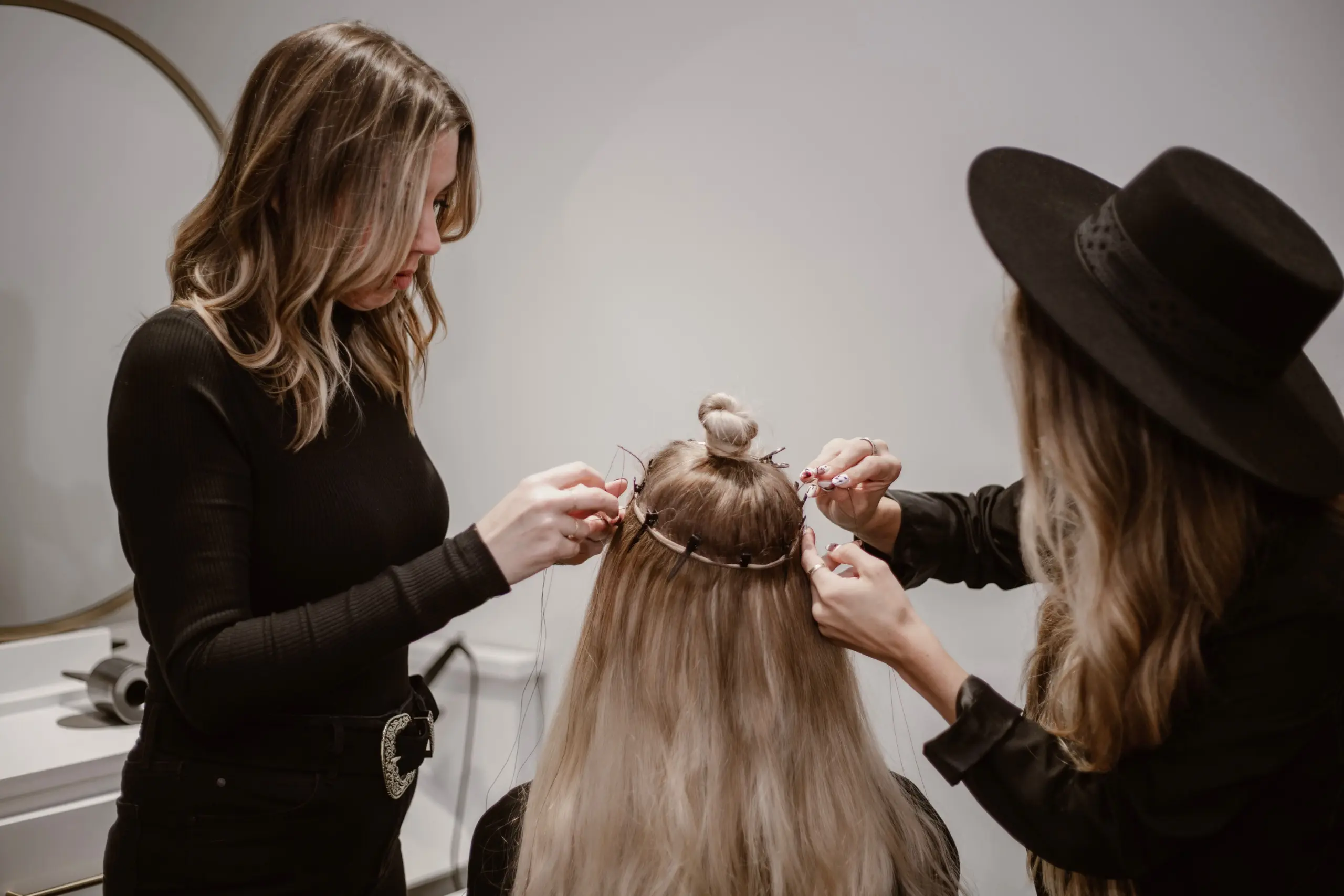 Two hair stylists applying hand-tied hair extensions on a client